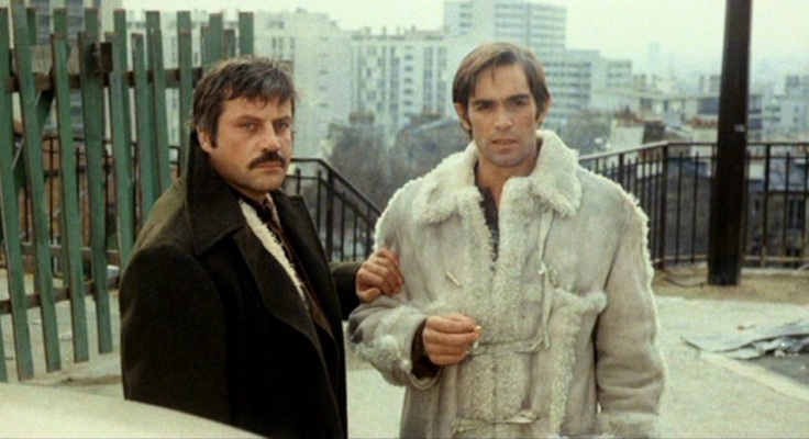 Oliver Reed im dunklen Anzug und Fabio Testi im weißen Pelz harren skeptisch der Dinge, die da noch kommen